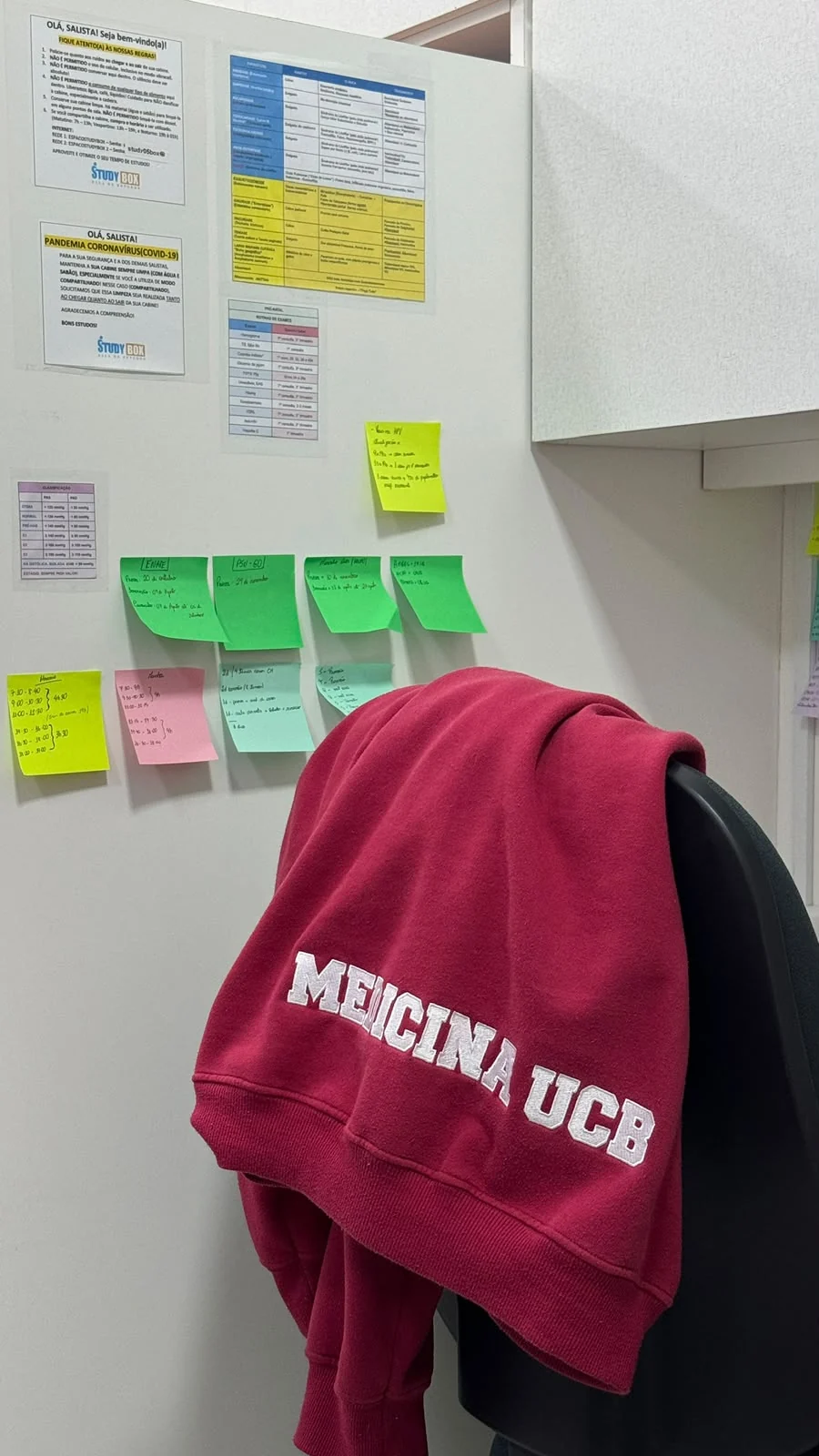 Cadeira de uma cabine com moletom de Medicina e post-its de estudo na parede