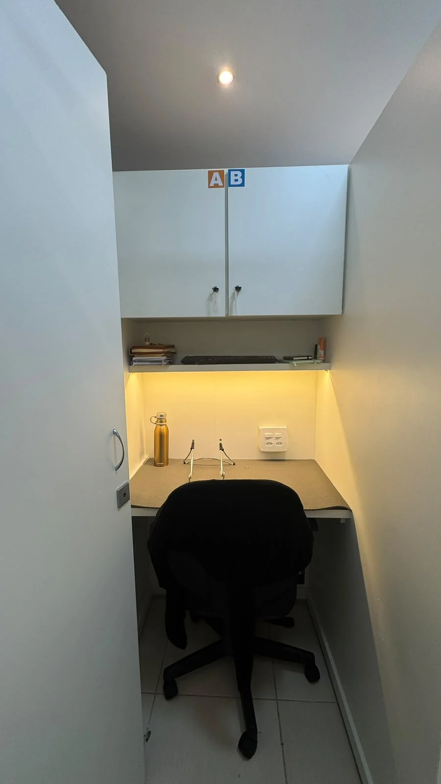 Interior de uma cabine VIP fechada, com armário, prateleira, iluminação quente e cadeira
